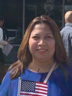Algebra 2 teacher Merceflor Kirk smiles for a picture outside the US Citizenship and Immigration Services Office while holding a miniature American flag in her hand. After getting her citizenship, Kirk told her family and friends about the great news.