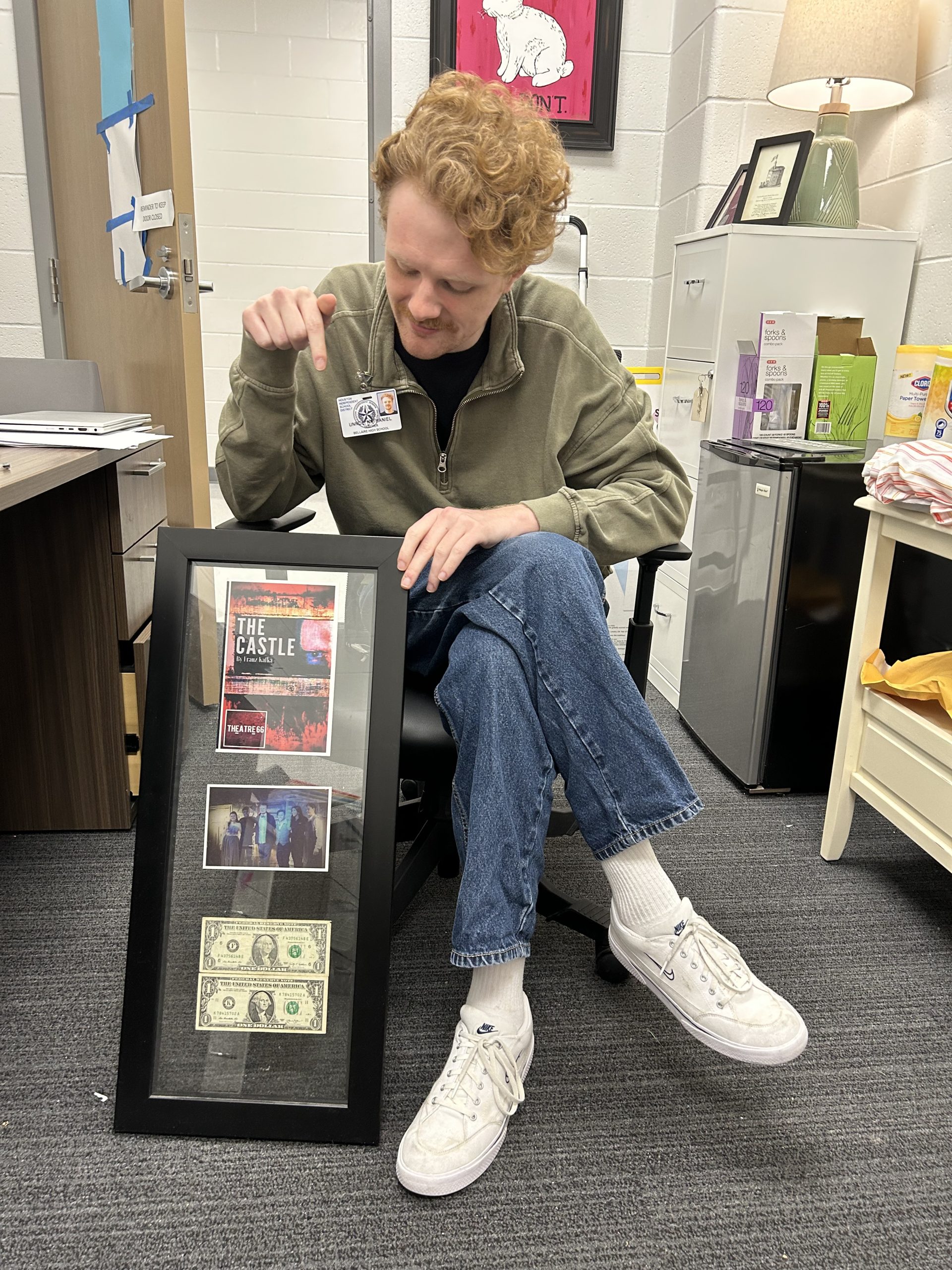 Theater teacher Nathaniel Unroe looks down at a picture frame of the playbill from the first play he ever directed, The Castle, a photo of the cast he worked with for the play and the first two dollars he ever earned while directing.