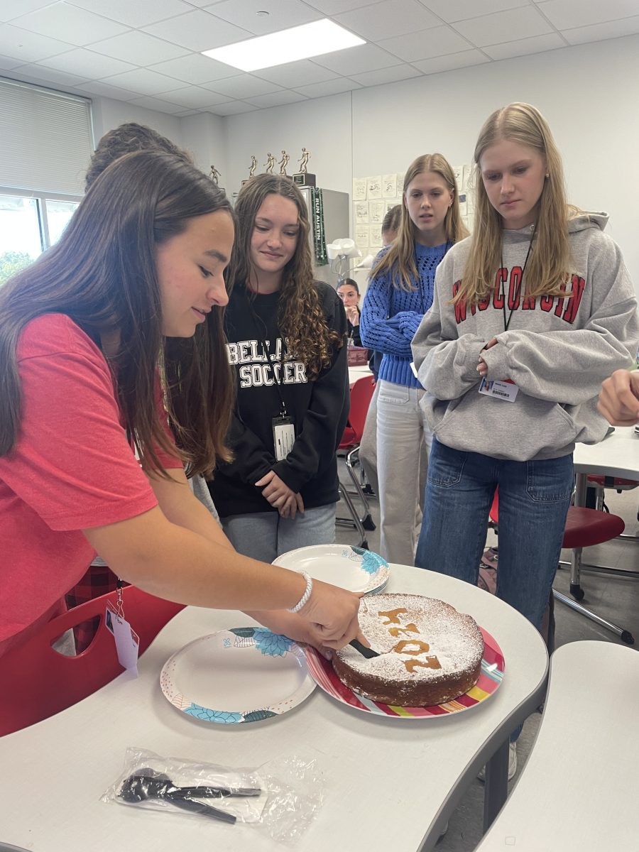 Allie Maglaras cuts one of two cakes for the Greek club meeting. Members CeCe Stampas and Grish Oomman found the coins hidden inside.