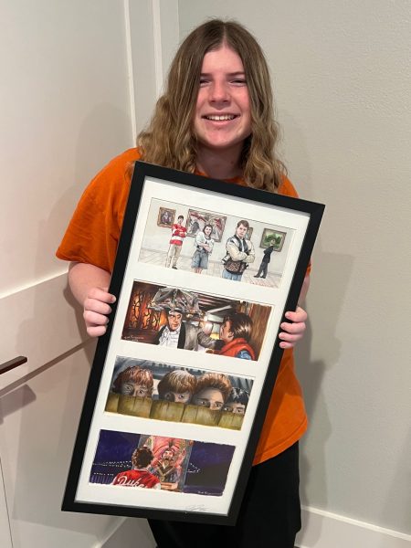 Sophomore Samantha Lepow holding a piece of framed artwork of some of her favorite movies from the 1980s. The movies pictured starting at the top are as follows: Ferris Buellers Day Off, Back to the Future, The Goonies, Big.