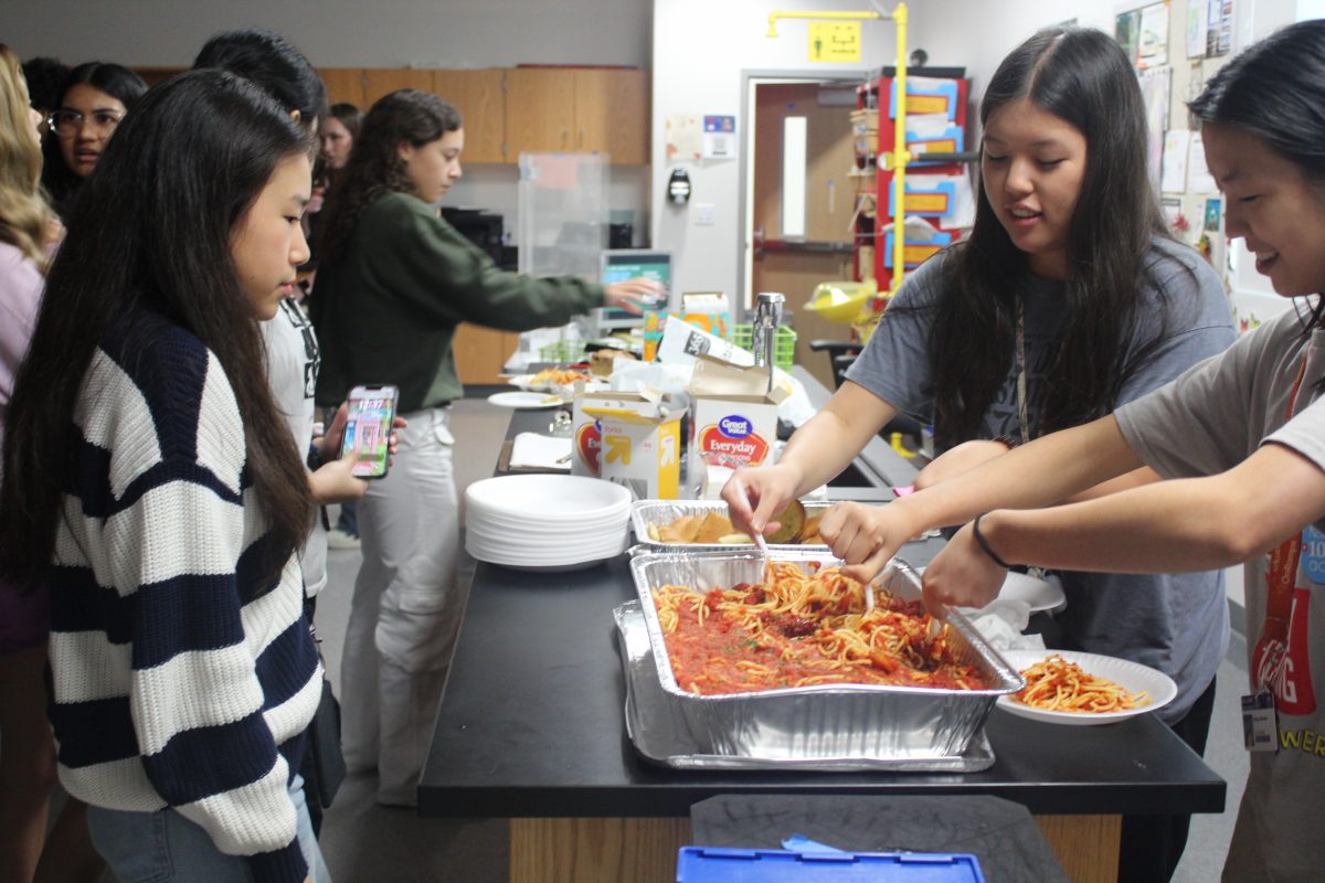 Junior Elyse Chiou and sophomore Miranda Wang prepare a plate of Pepperonis vegan pasta for sophomore Sydney Nguyen. The club assembled an array of vegan foods for the celebration.