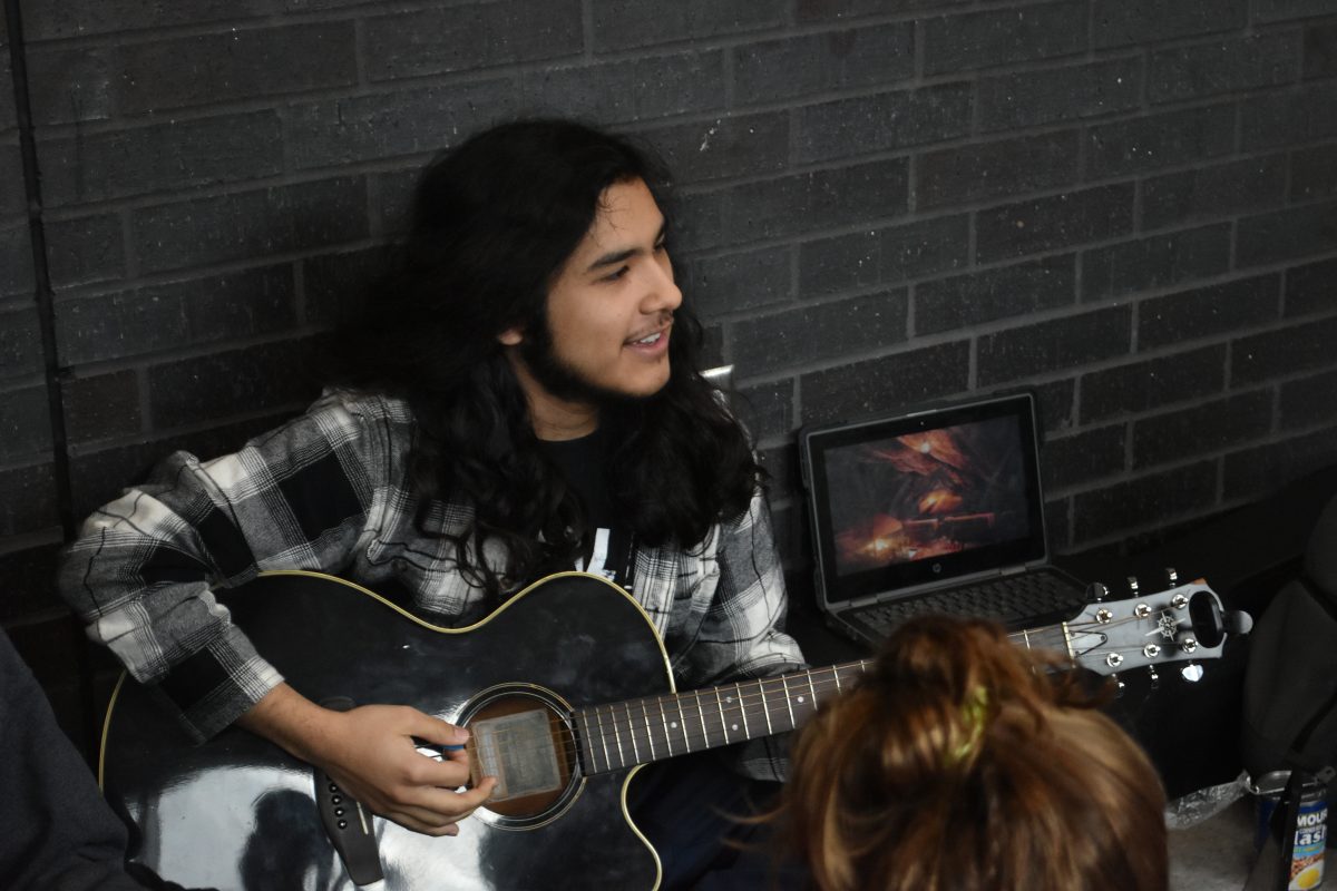 Senior+Raymond+Gamboa+plays+his+guitar+next+to+a+campfire+video+playing+on+his+laptop.+He+enjoys+playing+his+guitar+and+hanging+our+with+his+friends.