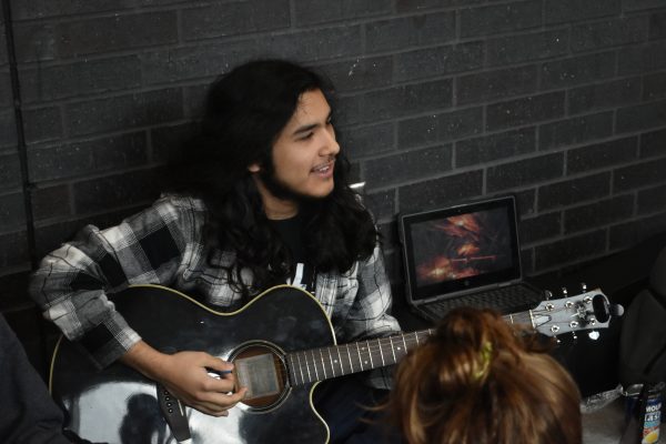 Senior Raymond Gamboa plays his guitar next to a campfire video playing on his laptop. He enjoys playing his guitar and hanging our with his friends.