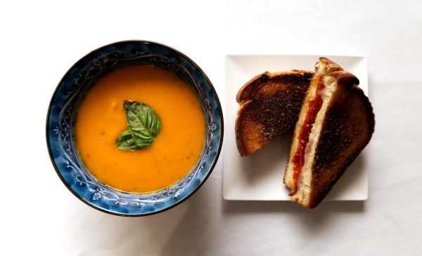 A bowl of tomato bisque is paired with a pepperoni grilled cheese brushed with garlic butter. The tomato bisque took around three hours to make, with the majority of time spent on reducing the soup.