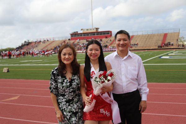 Nguyen stands with her parents during the Belles' senior night football game. Each Belle walks on the field with their parents holding a bouquet, celebrating their last year on the team.