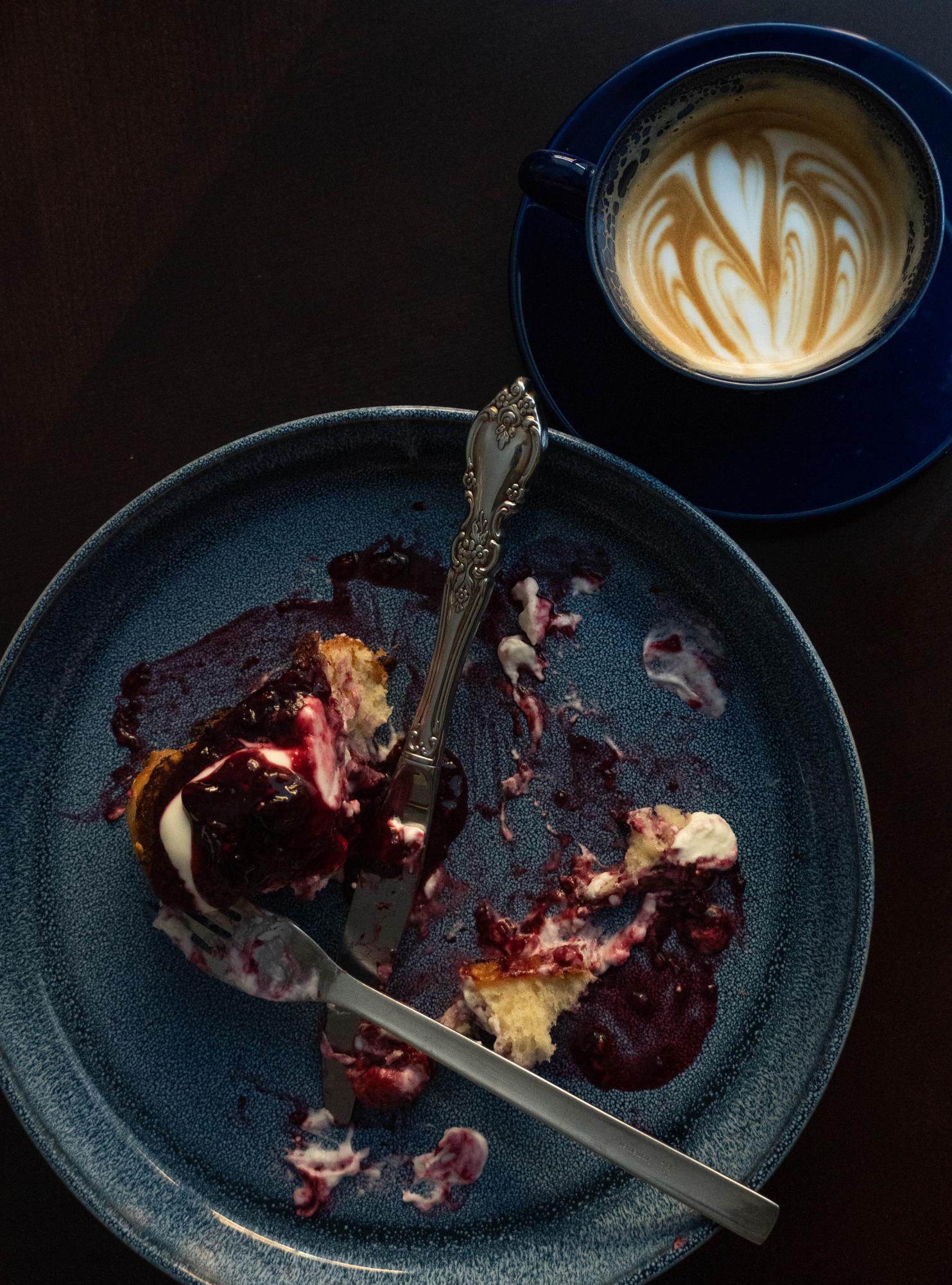 A half-eaten plate of mixed berry French toast sits beside a whole milk latte. The syrup used in the toast was made from a mix of blackberries, raspberries and blueberries after being macerated for 40 minutes.