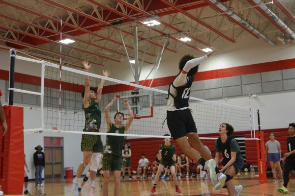 Varsity player senior Brain Scott (jersey number 12) prepares to spike the ball onto Strake Jesuit's side of the court. Strake Jesuit prepares to block the ball by reaching above the net.