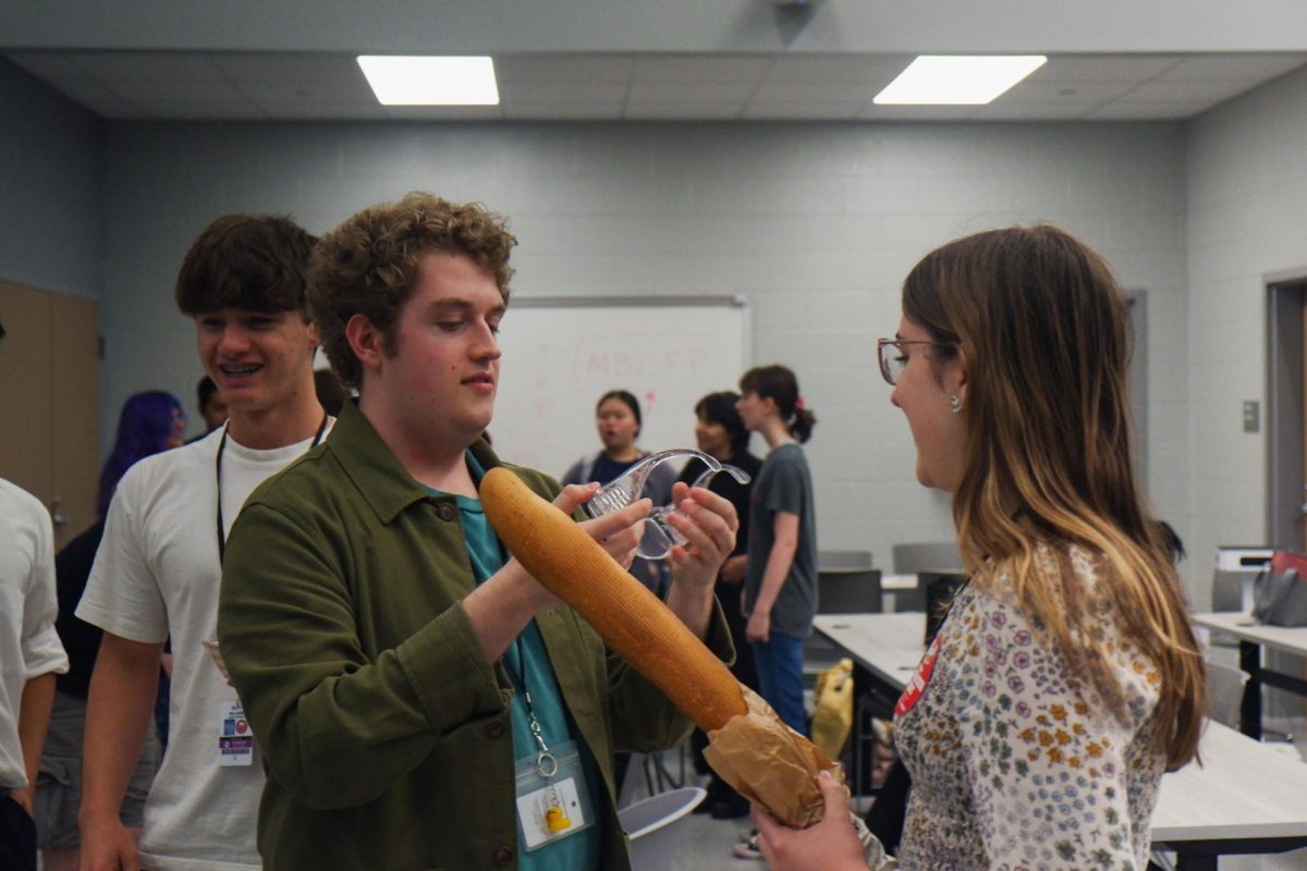 Bread Club President and senior Sam Dove helps a combatant put on safety goggles. Students participating in the fencing tournament had to sign a waiver and wear eye protection before fighting.