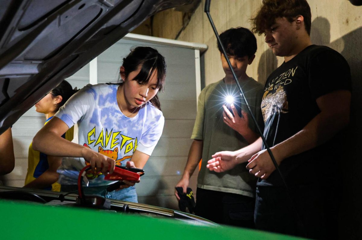 Co-president and senior Cathryn Vera jump-starts the art car while senior and engineering lead Alessandro Trevino and senior and finance lead Avery Tanzil assist. The car had to be jump-started to move it to the top floor of the garage.