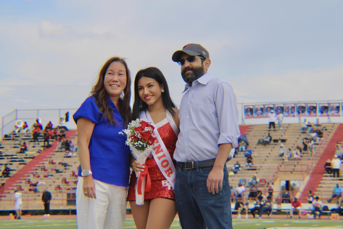 Anjali Kumar poses with her parents on the field while holding a bouquet and wearing her senior sash. She walked across the field during the senior game halftime ceremony.