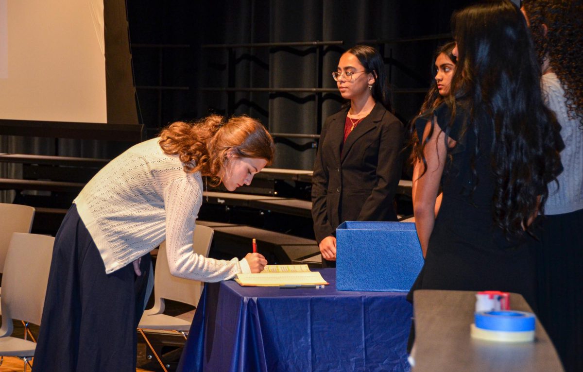 Junior Justine Finger signs the NHS logbook after walking the stage to receive her certificate. The logbook contains the name of every member and officer since the formation of the NHS.