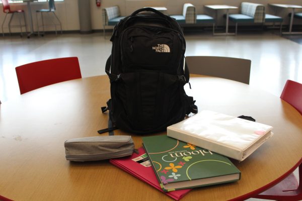 A backpack is on a desk with books laid around it. The one-bag policy has been in effect for a month.