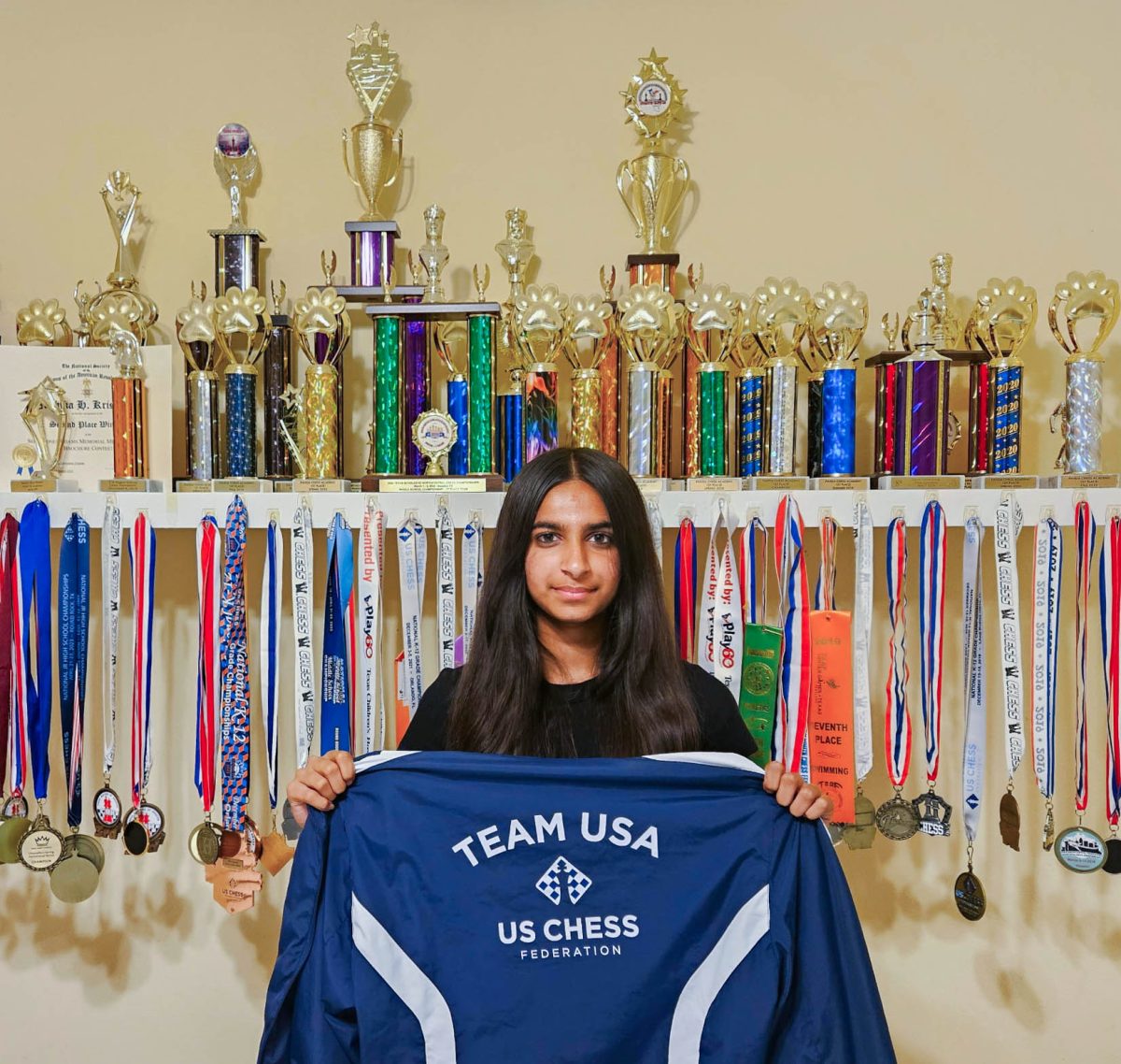 Krishnan displays the Team USA jacket, awarded to her at the Pan American Intercollegiate Chess Championship in Chicago. Rows of trophies lined the wall behind her, symbolizing her dedication to chess.
