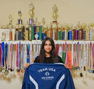 Krishnan displays the Team USA jacket, awarded to her at the Pan American Intercollegiate Chess Championship in Chicago. Rows of trophies lined the wall behind her, symbolizing her dedication to chess.